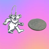 Silver bear-shaped earring next to a quarter on a gradient background